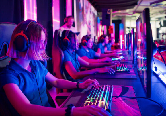 Diverse gamer group with african ethnicity female players playing competitive computer game in a gaming room. Wearing headset and talking into the microphone to communicate with the pro team and the coach.